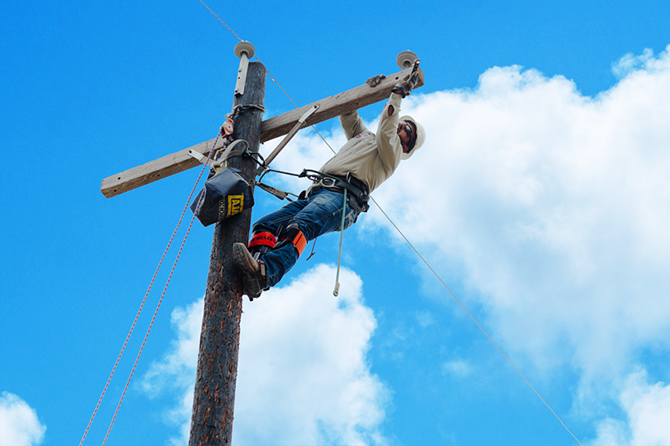 Lineman inspecting the wiring on a pole while secured to safety equipment.