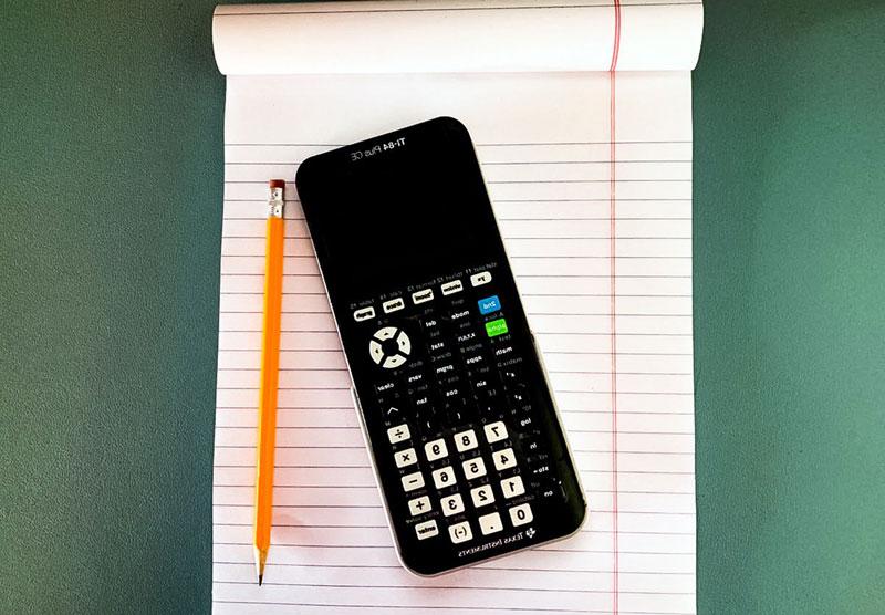 graphing calculator on desk with notebook and pencil