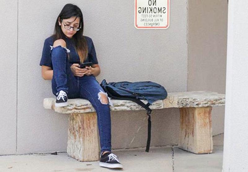 female student sitting on an outdoor bench looking at cellphone