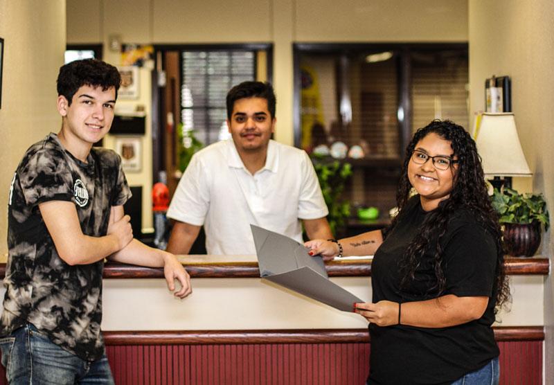 Three students reviewing papers with clerk at counter